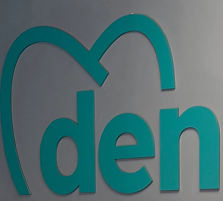 Letras del logo de Denxal en color teal sobre un muro gris de la clínica